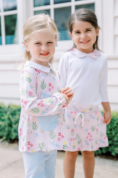 Two young girls wearing matching floral outfits standing outdoors.