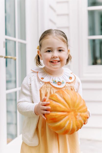 Young girl holding a pumpkin in front of a white door