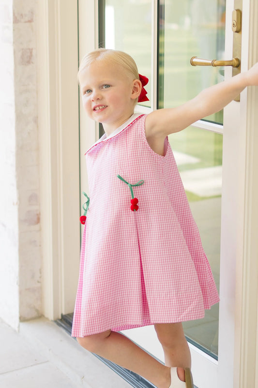 Young girl in a pink dress with red accents standing by a door.