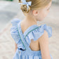 Young girl wearing a blue checkered dress with ruffled sleeves and a bow in her hair.