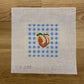 Cross-stitched peach design on fabric with blue and white checkered pattern