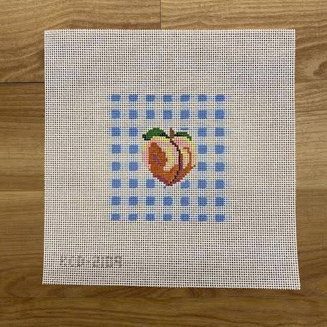 Cross-stitched peach design on fabric with blue and white checkered pattern