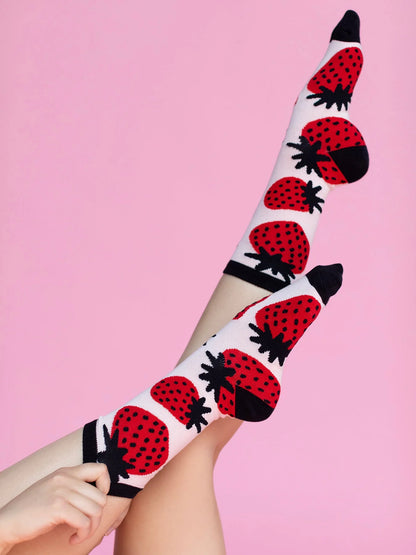 White knee-high socks with red strawberry pattern worn by a person on a pink background