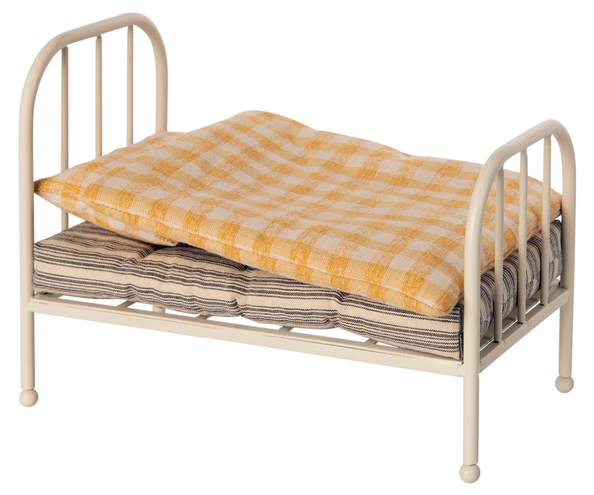 A small metal doll bed with a cream-colored frame, shown with a yellow-and-white checkered quilt and a striped mattress on a plain white background.