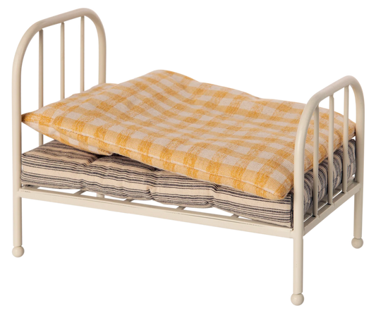 A small metal doll bed with a cream-colored frame, shown with a yellow-and-white checkered quilt and a striped mattress on a plain white background.