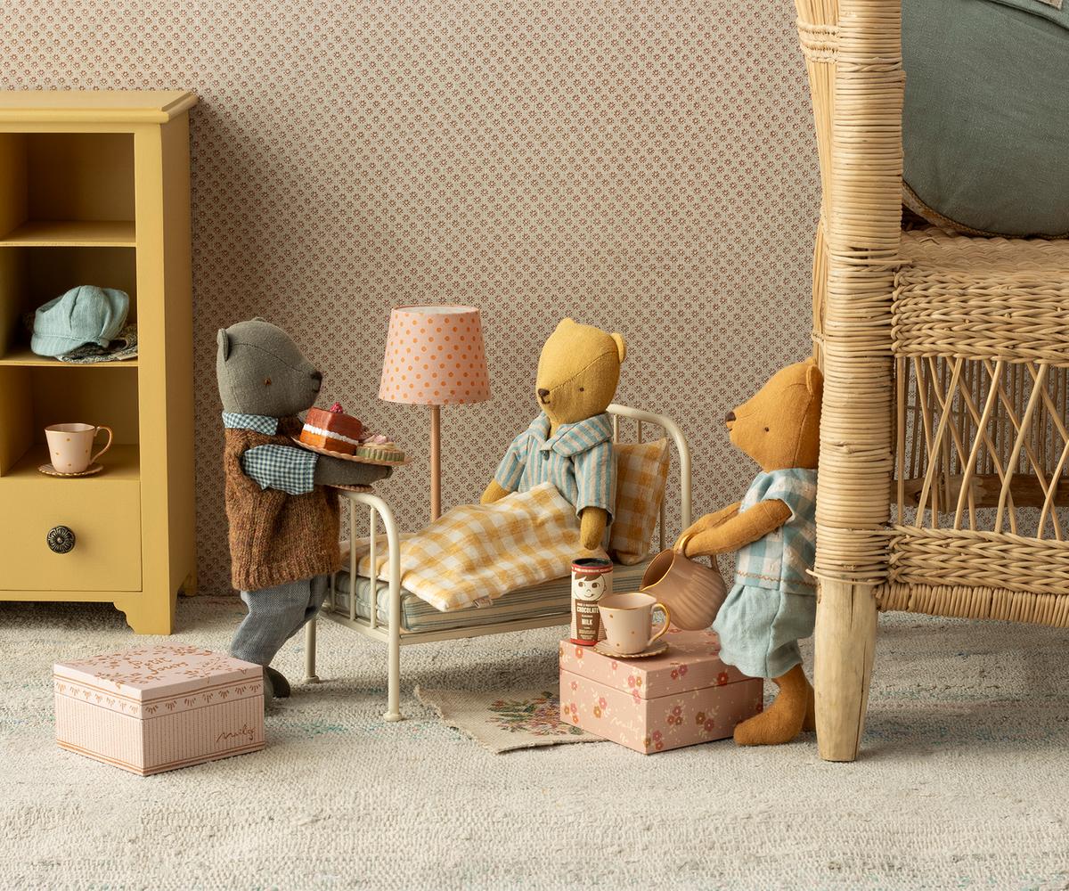 Toy bears in a room with furniture and decor, including a lamp and books.