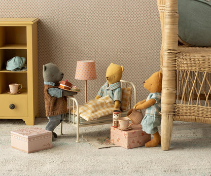 Toy bears in a room with furniture and decor, including a lamp and books.