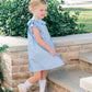 Young girl in a light blue dress standing on steps outdoors with greenery in the background
