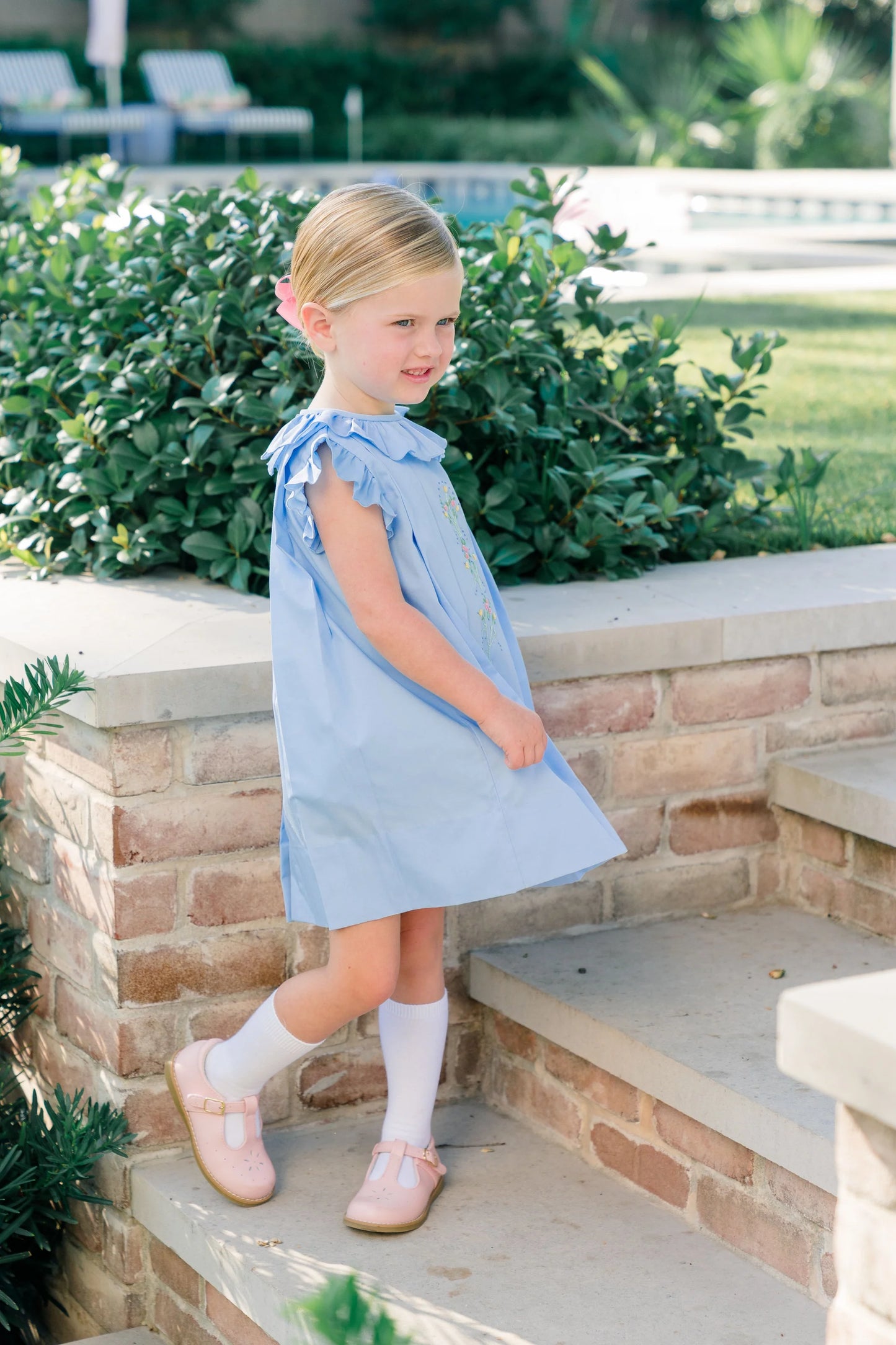Young girl in a light blue dress standing on steps outdoors with greenery in the background