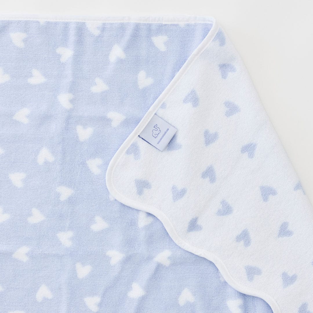 Baby blanket with heart pattern and brand tag on a light blue background