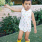 Child wearing a sleeveless dress with sailboat pattern and yellow rain boots outdoors.