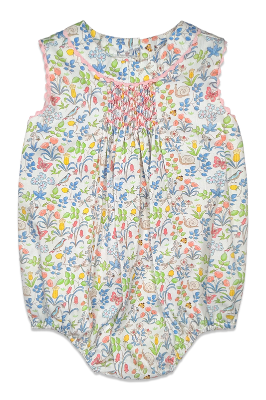 A sleeveless baby romper with a colorful floral and butterfly print on a white background, featuring smocked detailing at the chest.