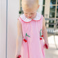 Young girl wearing a pink checkered dress with cherry details outdoors.