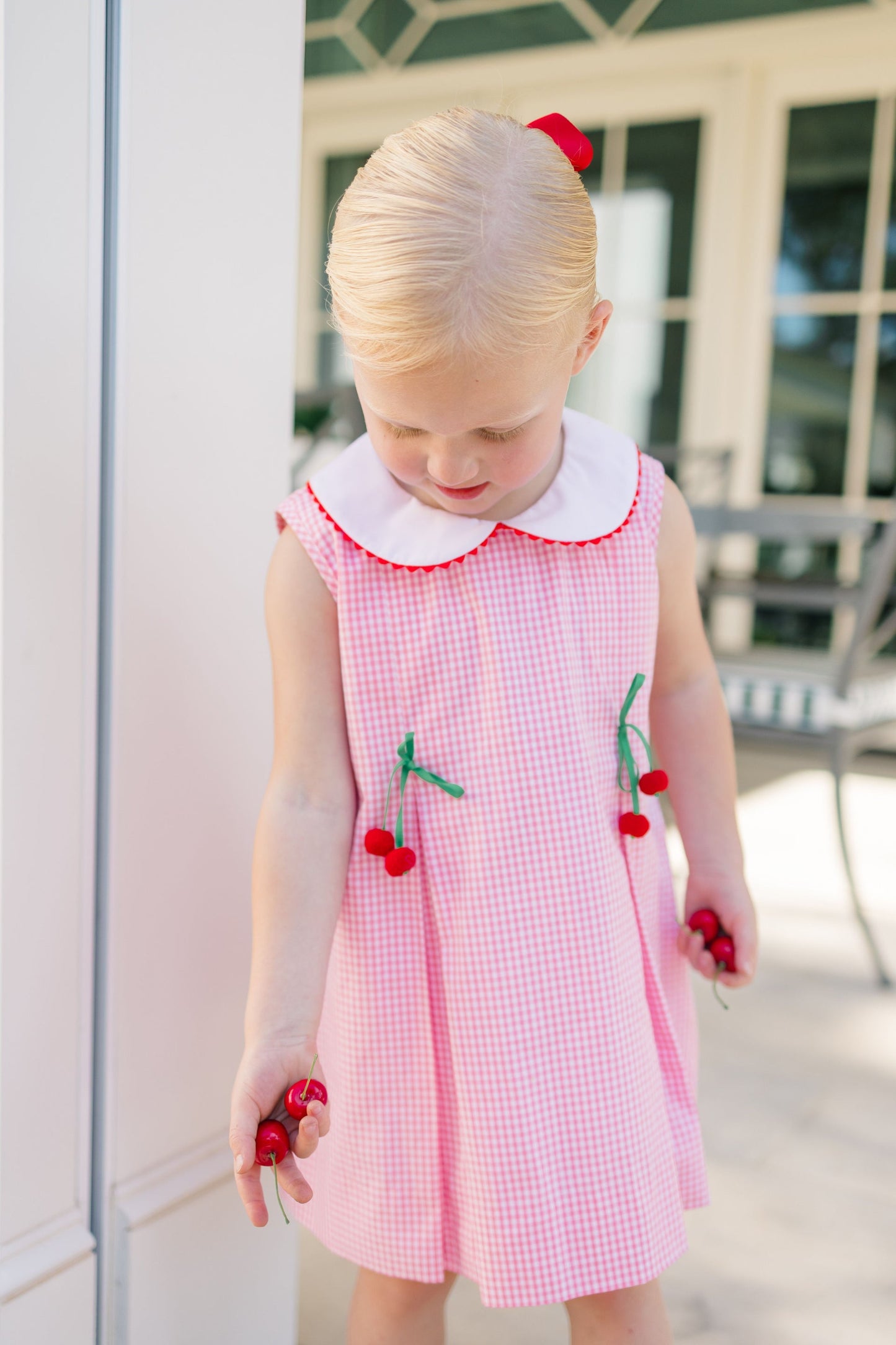 Young girl wearing a pink checkered dress with cherry details outdoors.