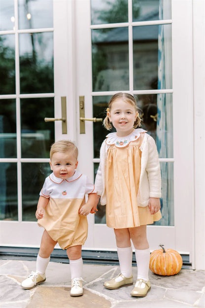 Two children in matching outfits standing in front of a glass door with a pumpkin on the ground.