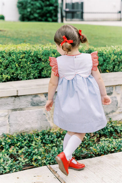 Child wearing a blue and white dress with red accents, standing outdoors.
