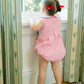 Child in a pink checkered dress standing by a window with patterned curtains.