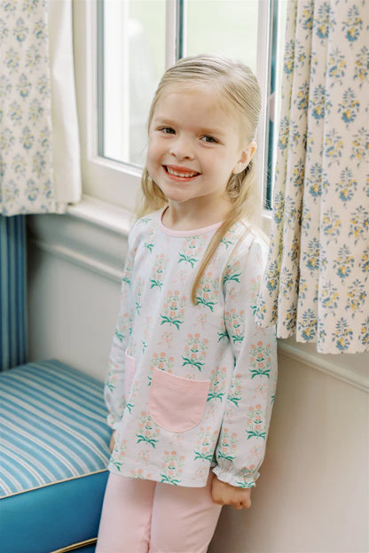 Young girl in a floral pajama set standing in a room with floral curtains.